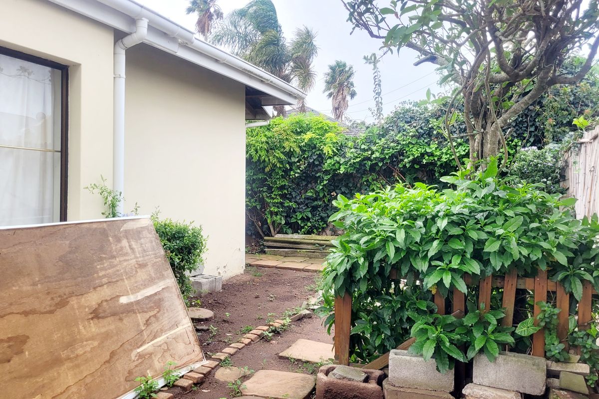 Rear exterior view of the property featuring a garden area with paving, retaining wall, and established vegetation along the boundary.