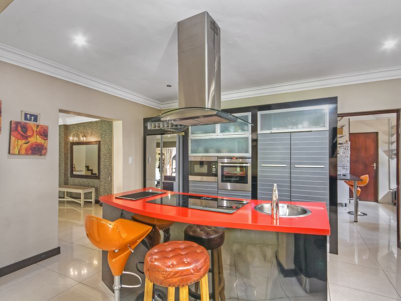 Modern kitchen featuring a central island with a red countertop, integrated appliances, stainless steel extractor fan, and polished tiled flooring.