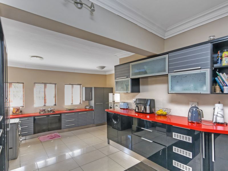 Spacious kitchen featuring modern high-gloss cabinetry, vibrant red countertops, tiled flooring, and integrated laundry facilities with ample natural light.