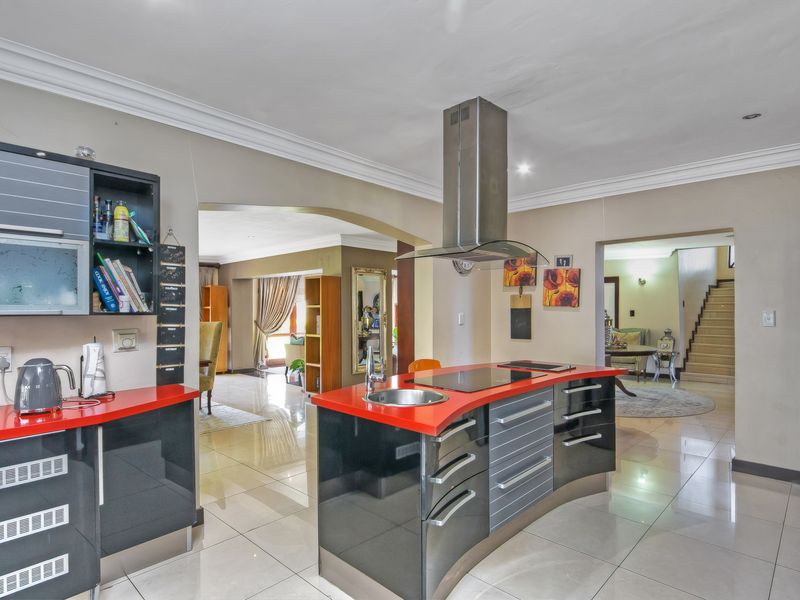 Modern kitchen featuring a curved island with a built-in hob, stainless steel extractor fan, and high-gloss cabinetry, flowing into the adjacent living areas.
