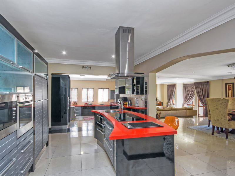 Spacious open-plan kitchen featuring a modern island with a red countertop, integrated appliances, and sleek cabinetry, flowing into the adjacent living and dining areas.