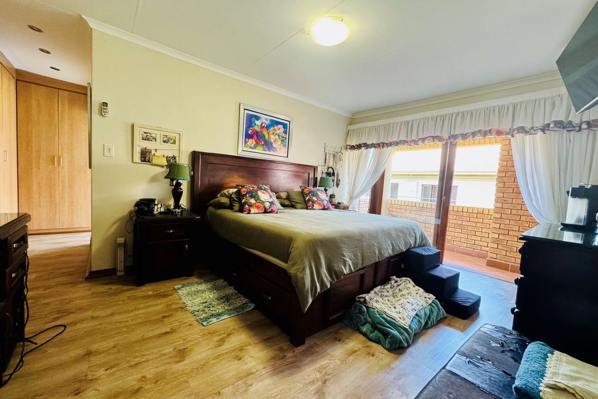 Spacious bedroom featuring wood-look laminate flooring, built-in cupboards, and sliding glass doors providing direct access to a private balcony.
