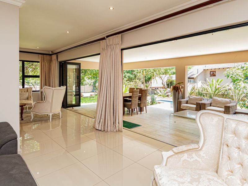 Spacious open-plan living area featuring large stacking glass doors that seamlessly connect the interior to a covered outdoor patio and garden.