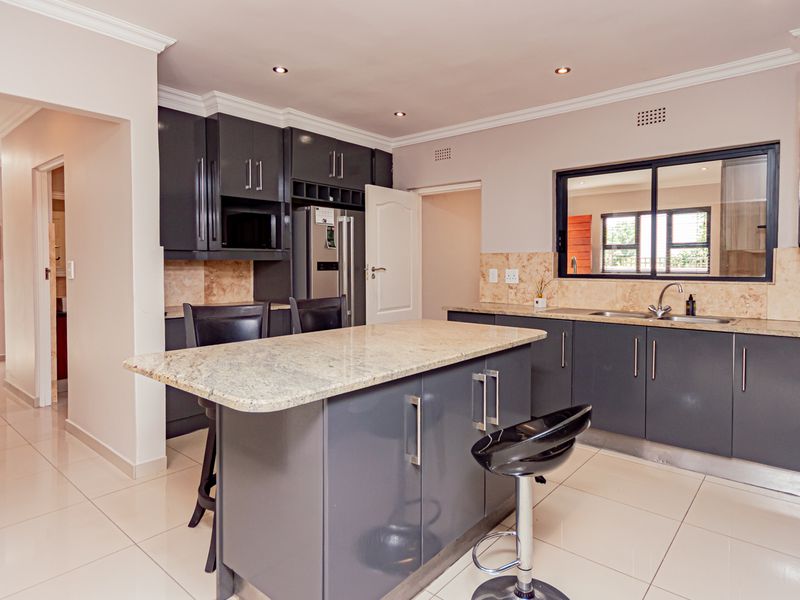 Modern kitchen featuring dark cabinetry, granite countertops, a central island, and tiled flooring, offering a functional and contemporary cooking space.
