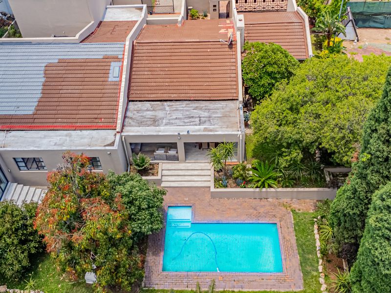 Aerial view of the property featuring a swimming pool, paved patio area, and mature garden landscaping with a multi-section tiled roof.