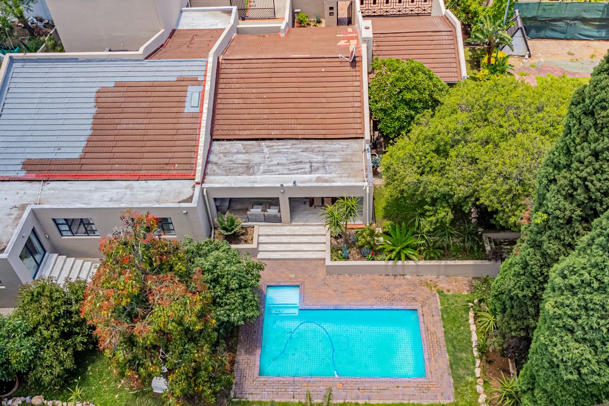 Aerial view of the property featuring a swimming pool, paved patio area, and mature garden landscaping with a multi-section tiled roof.