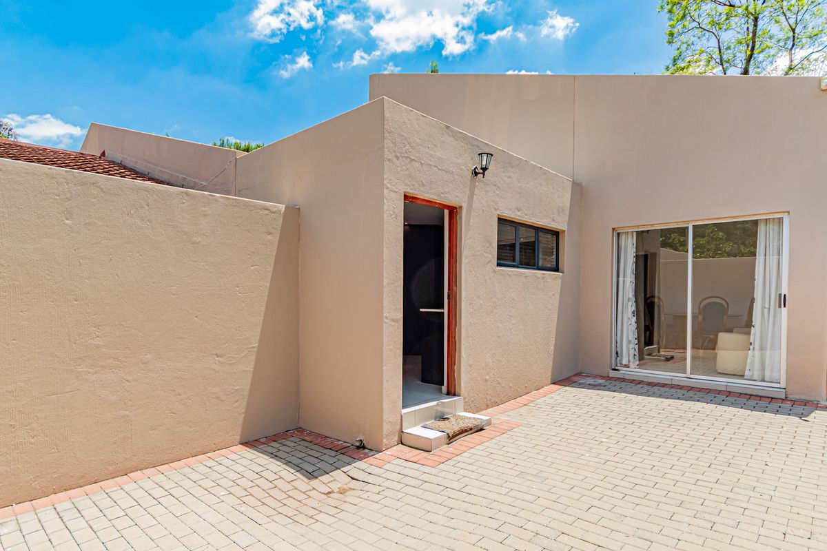 A paved rear courtyard area featuring a sliding glass door entrance and a clean, modern exterior facade.