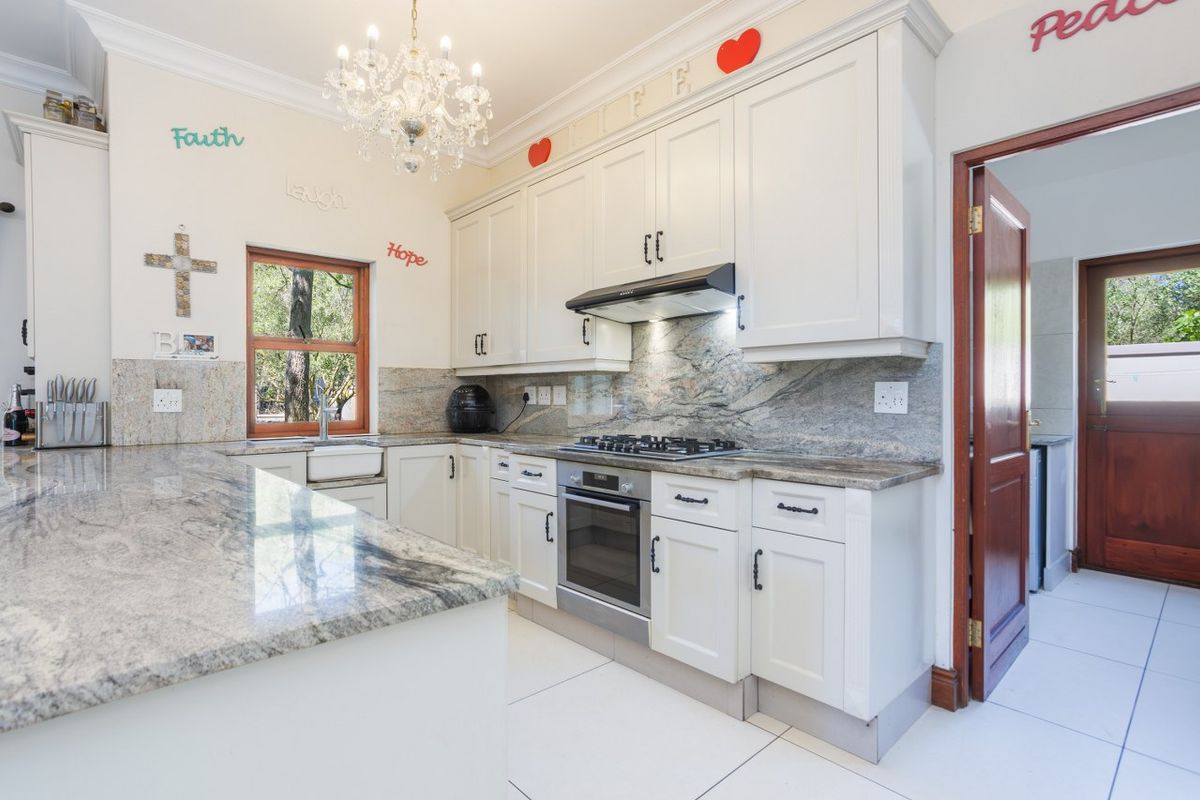 A well-appointed kitchen featuring granite countertops, white cabinetry, a built-in oven with gas hob, extractor fan, and a farmhouse-style sink.