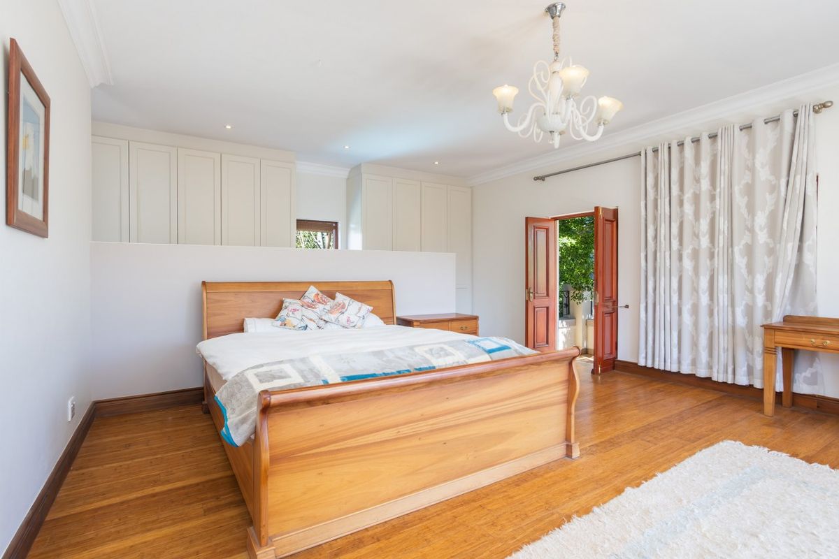 Spacious bedroom featuring polished timber flooring, built-in cabinetry, recessed downlighting, and direct access to an outdoor area through double doors.