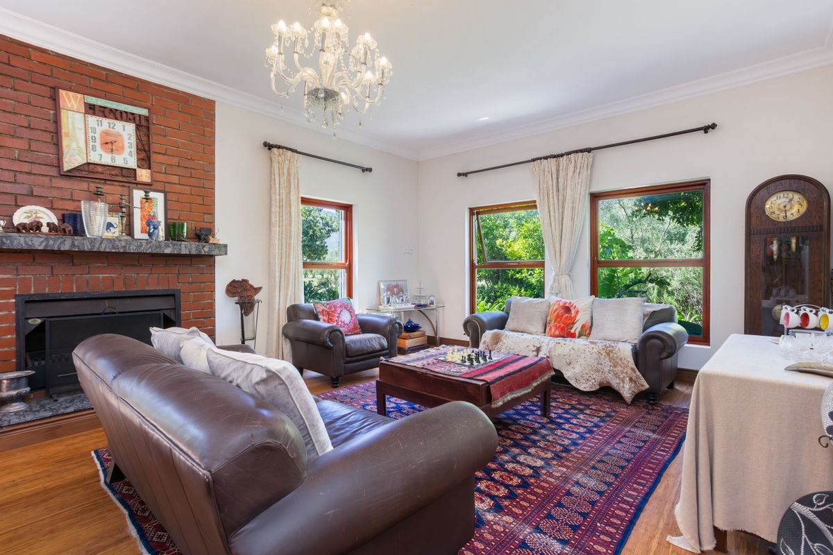 Spacious living room featuring a classic red brick fireplace, timber flooring, and large windows overlooking the garden.