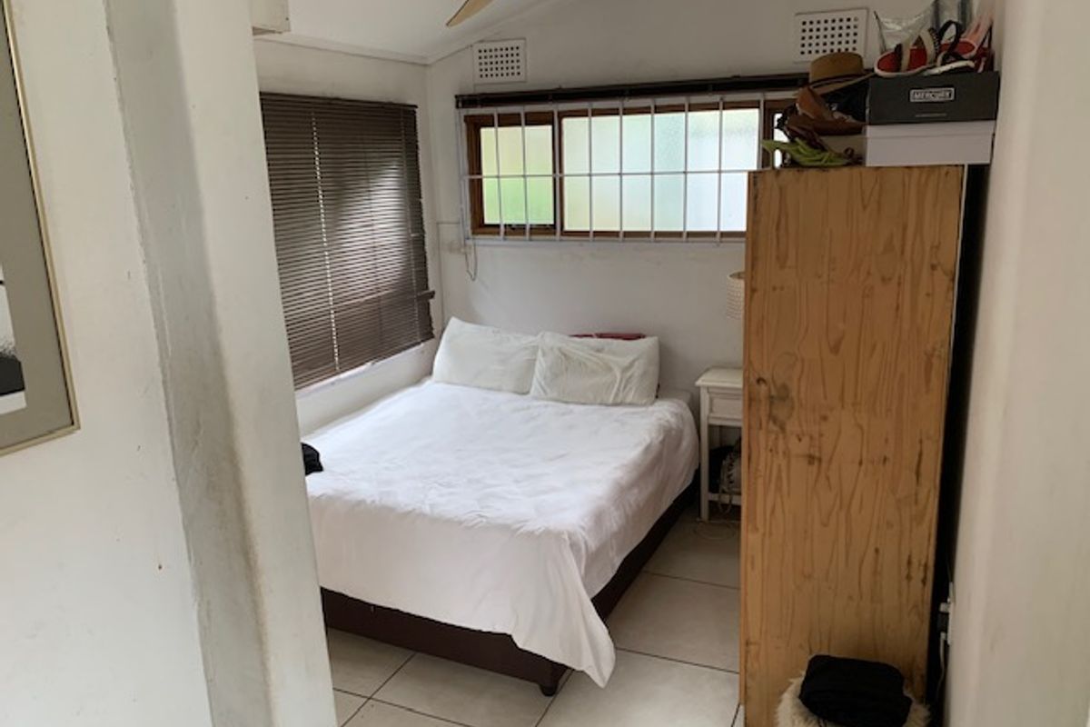 A compact bedroom featuring tiled flooring, a ceiling fan, and security bars on the windows. The space requires cosmetic updates to improve its overall condition.