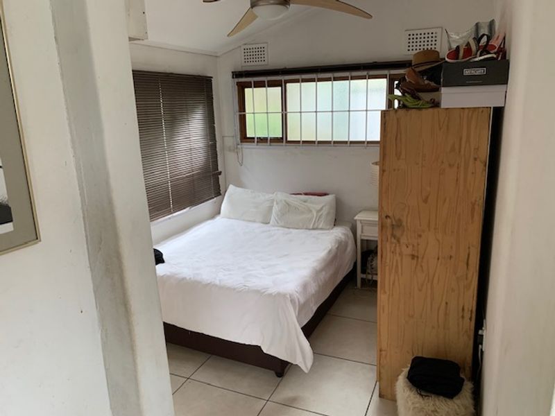 A compact bedroom featuring tiled flooring, a ceiling fan, and security bars on the windows. The space requires cosmetic updates to improve its overall condition.