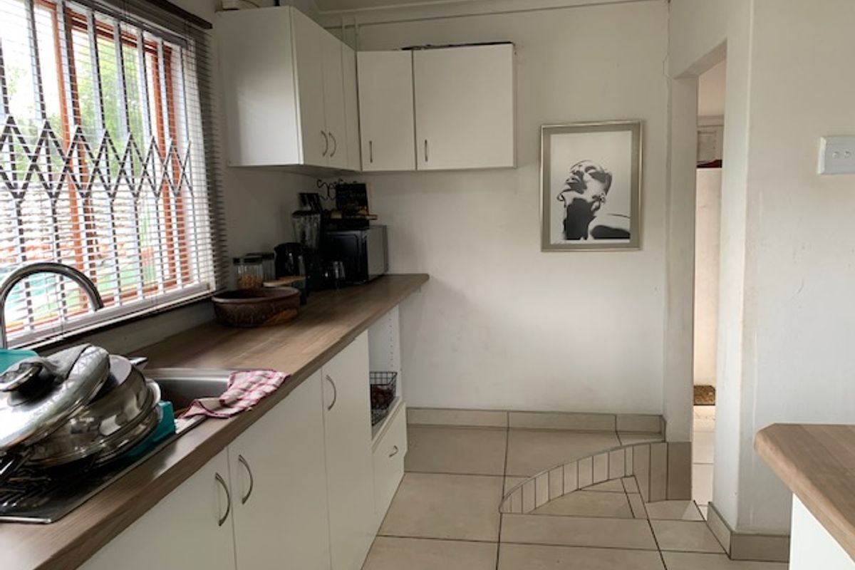 A functional kitchen featuring white cabinetry, wood-look laminate countertops, stainless steel sink, and tiled flooring with a view through security-barred windows.