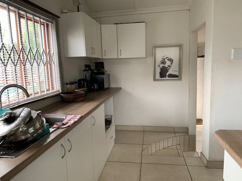 A functional kitchen featuring white cabinetry, wood-look laminate countertops, stainless steel sink, and tiled flooring with a view through security-barred windows.