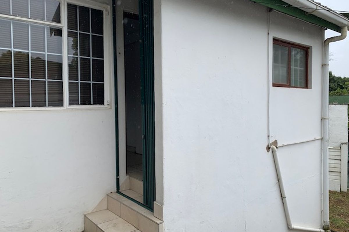 Rear exterior view of the cottage featuring tiled entrance steps, security gate, and visible downpipe infrastructure.