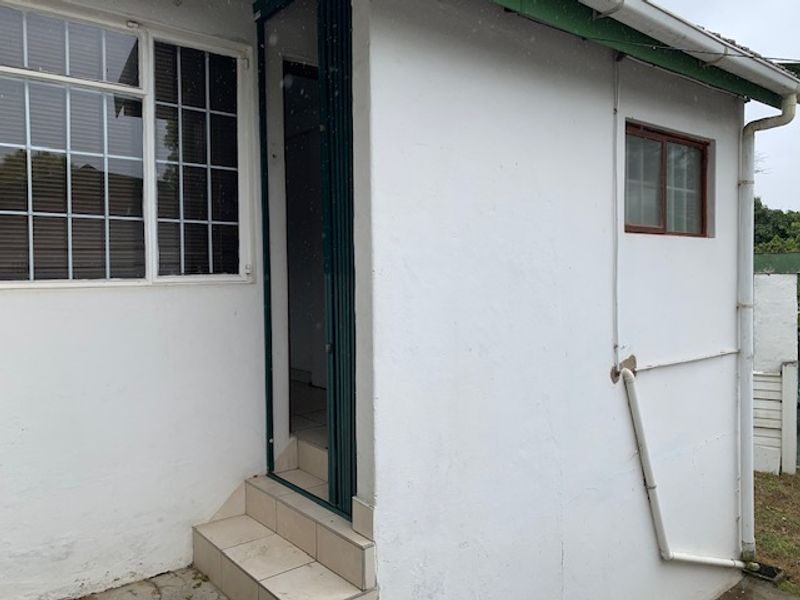 Rear exterior view of the cottage featuring tiled entrance steps, security gate, and visible downpipe infrastructure.