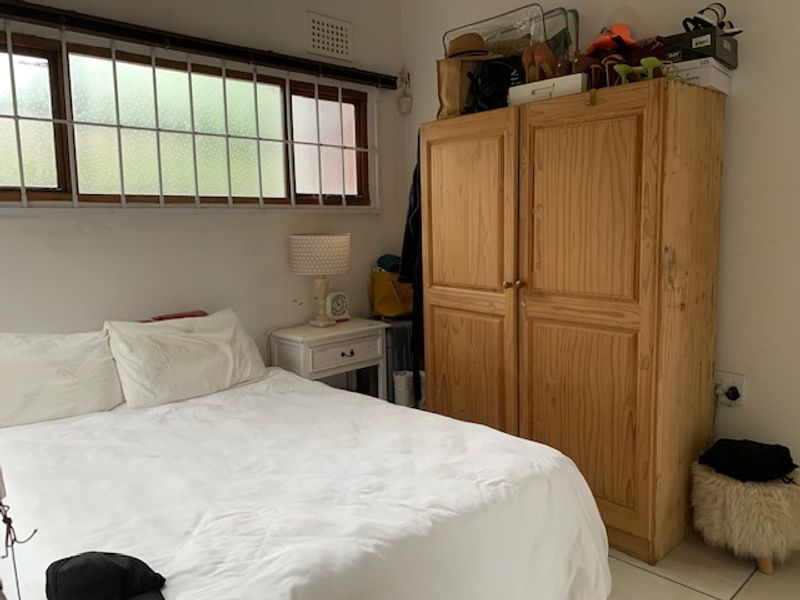 A functional bedroom featuring tiled flooring, a window with security bars, and a built-in ventilation grille.