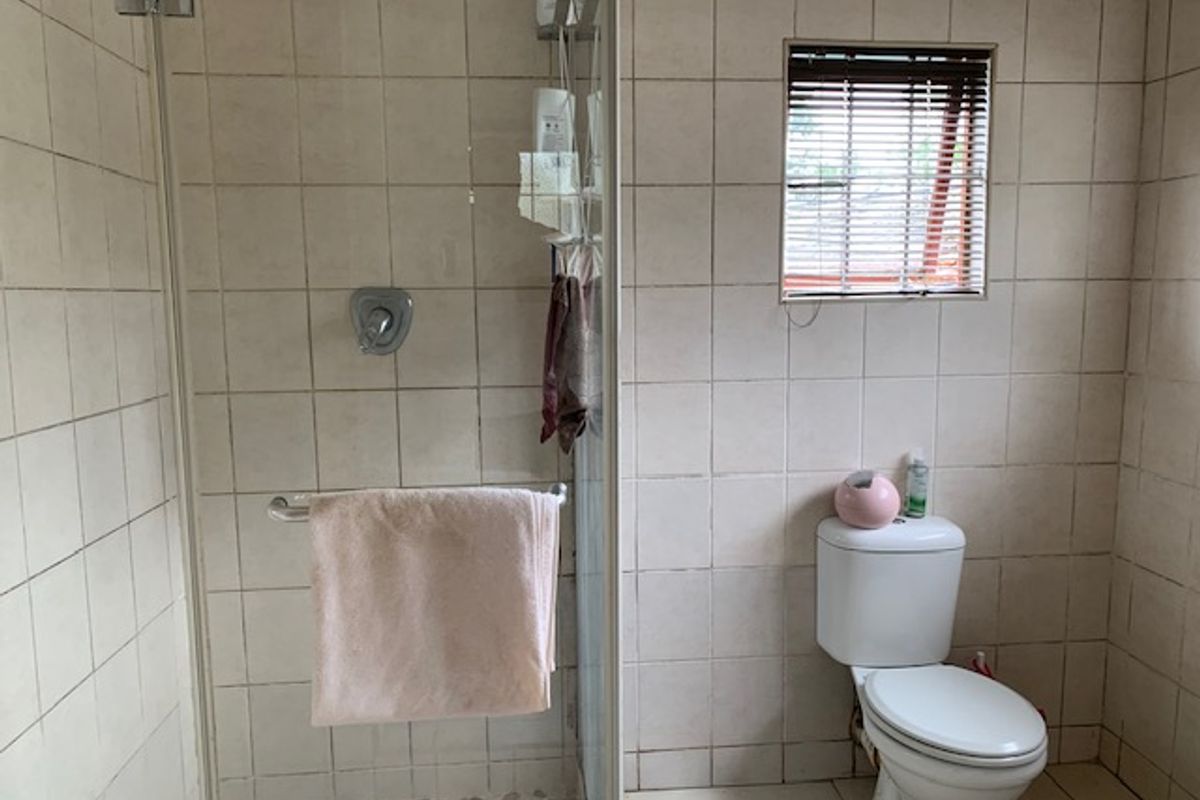 A functional bathroom featuring a glass-enclosed shower, a standard toilet, and neutral wall tiling, offering a practical layout with potential for cosmetic updates.
