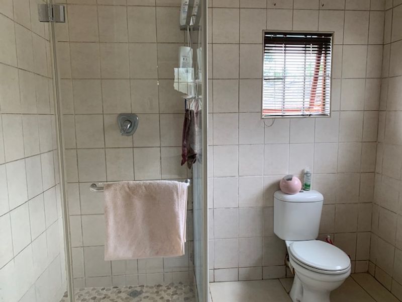 A functional bathroom featuring a glass-enclosed shower, a standard toilet, and neutral wall tiling, offering a practical layout with potential for cosmetic updates.