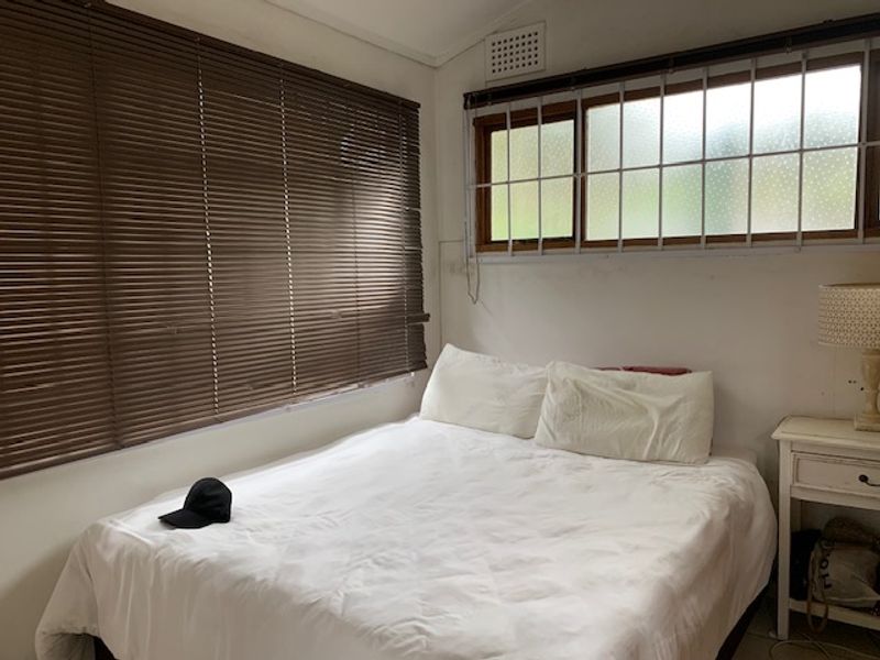 A compact bedroom featuring security bars on the windows and venetian blinds, requiring minor cosmetic updates to refresh the space.