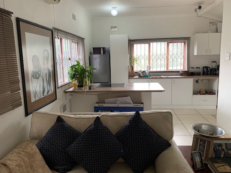 Open plan living and kitchen area featuring tiled floors, white cabinetry, and security bars on windows, offering a functional and connected living space.