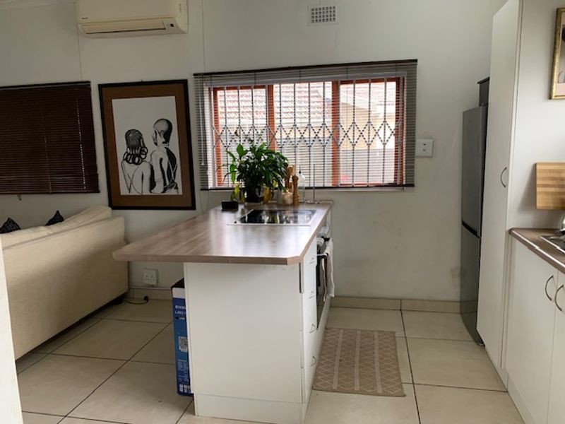Open plan living and kitchen area featuring a central island with built-in cooktop, tiled flooring, and split-system air conditioning.