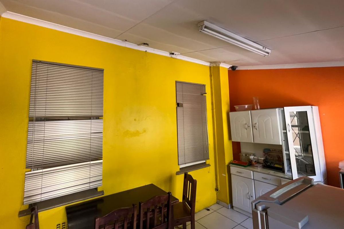 A kitchen area featuring built-in cabinetry, tiled flooring, and fluorescent lighting, currently requiring cosmetic updates to the wall finishes.