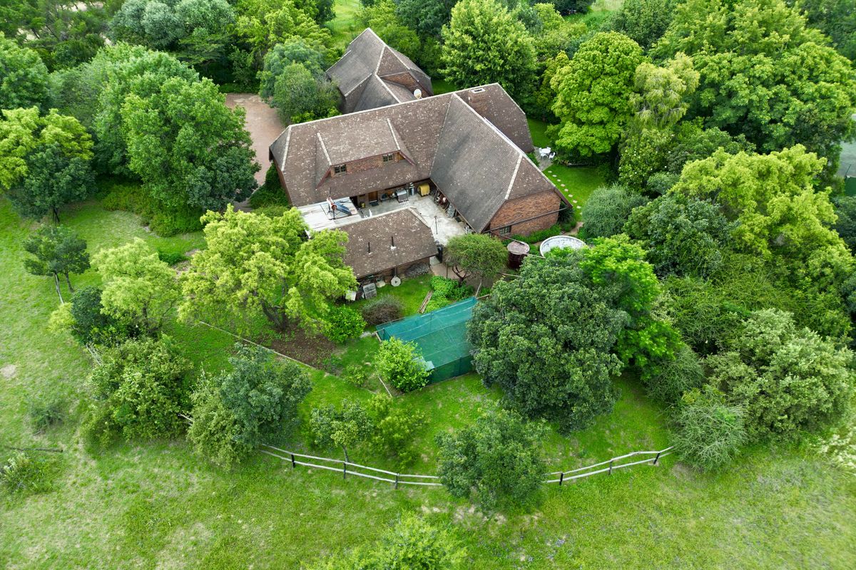 Aerial view of a large residential property featuring a multi-pitched tiled roof, surrounded by extensive mature trees and landscaped garden areas.