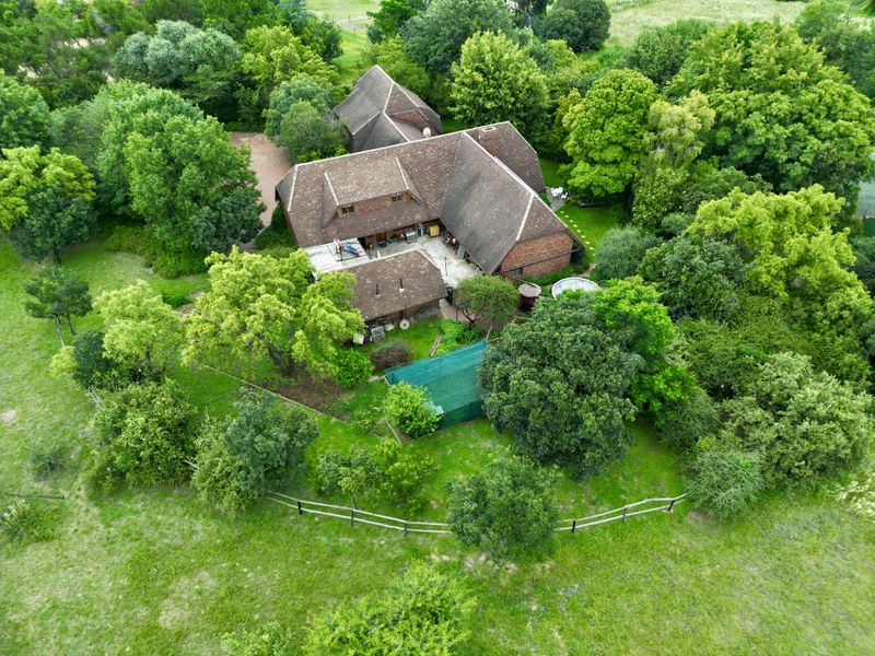 Aerial view of a large residential property featuring a multi-pitched tiled roof, surrounded by extensive mature trees and landscaped garden areas.