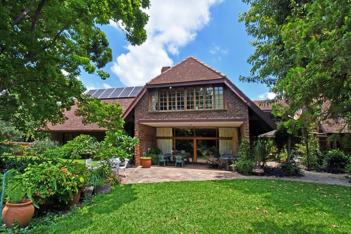 A view of the rear facade featuring a brick exterior, tiled roof, solar panels, and a paved patio area overlooking a lush garden.