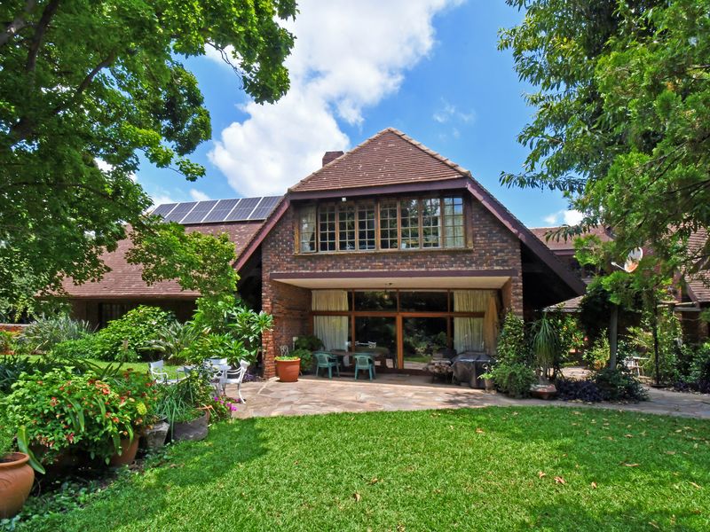 A view of the rear facade featuring a brick exterior, tiled roof, solar panels, and a paved patio area overlooking a lush garden.