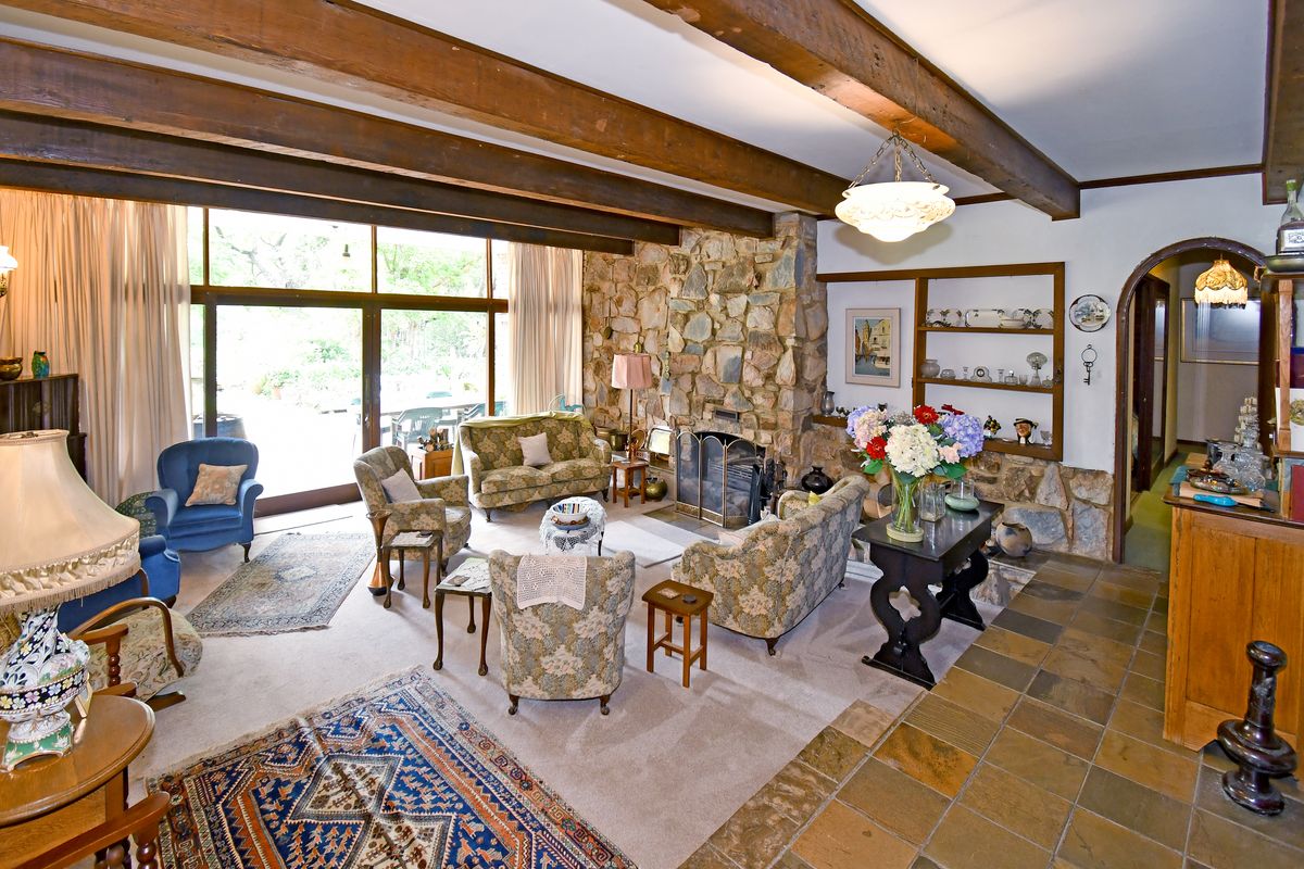 Spacious living room featuring exposed timber ceiling beams, a prominent stone fireplace, and large sliding glass doors opening to the garden.