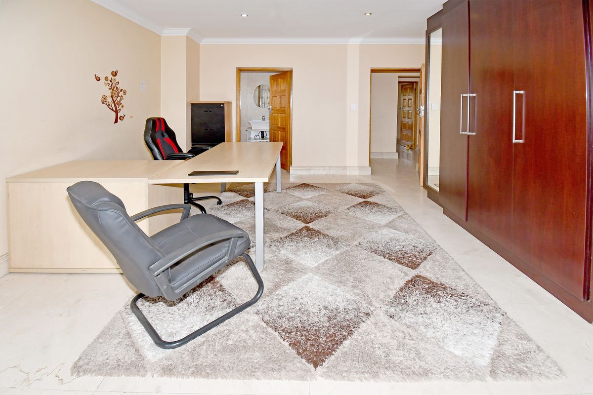 Spacious bedroom featuring built-in wardrobes, tiled flooring, and recessed downlights, with an adjoining en-suite bathroom visible through the doorway.