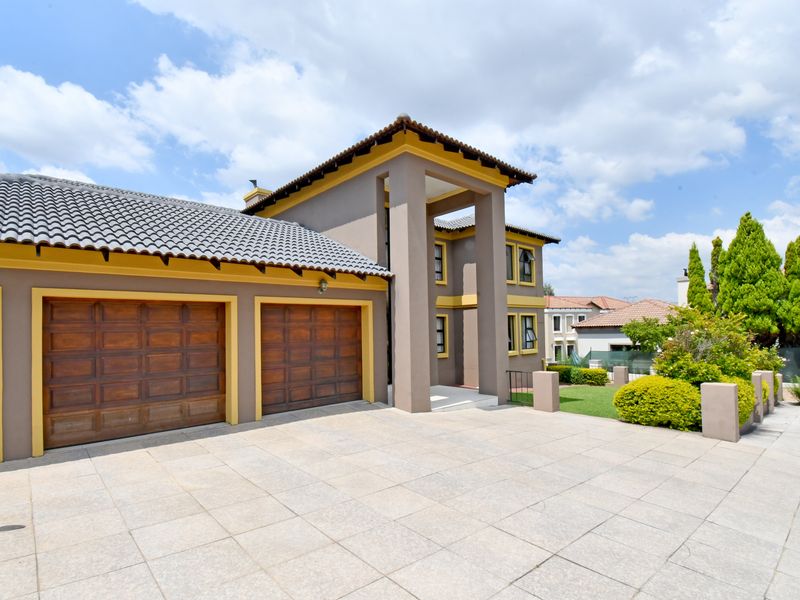 A well-maintained double-storey residence featuring a paved driveway, double garage, and a prominent architectural entrance with concrete pillars.
