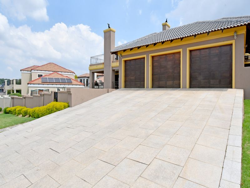 A well-maintained residential property featuring a spacious triple garage, a paved driveway, and a tiled roof with an elevated balcony.