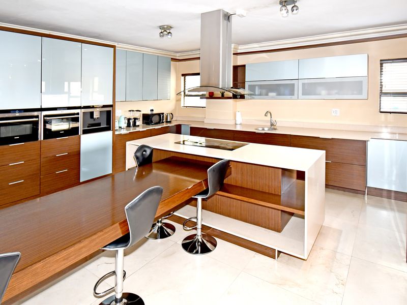 Modern kitchen featuring high-gloss cabinetry, a central island with integrated cooktop, stone countertops, and built-in appliances, finished with polished floor tiles.