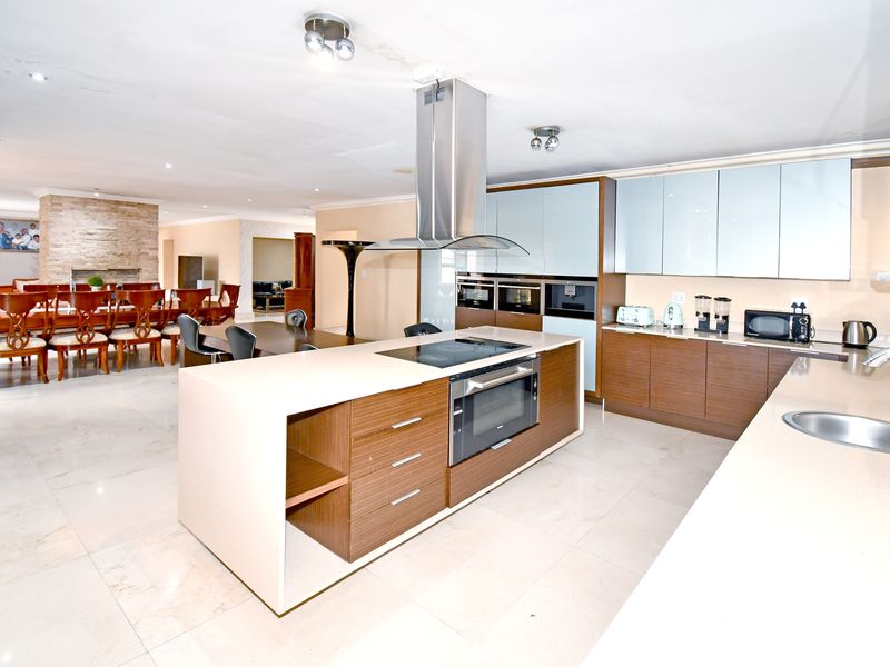 Spacious open-plan kitchen and dining area featuring a central island, modern cabinetry, stone countertops, and a stone feature wall in the dining space.