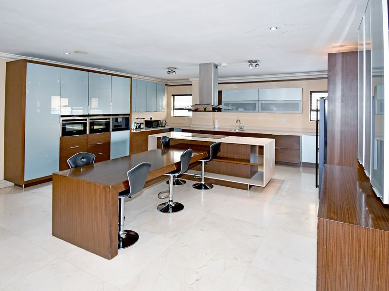 Modern kitchen featuring integrated cabinetry, built-in ovens, a central island with breakfast bar seating, and stone countertops.