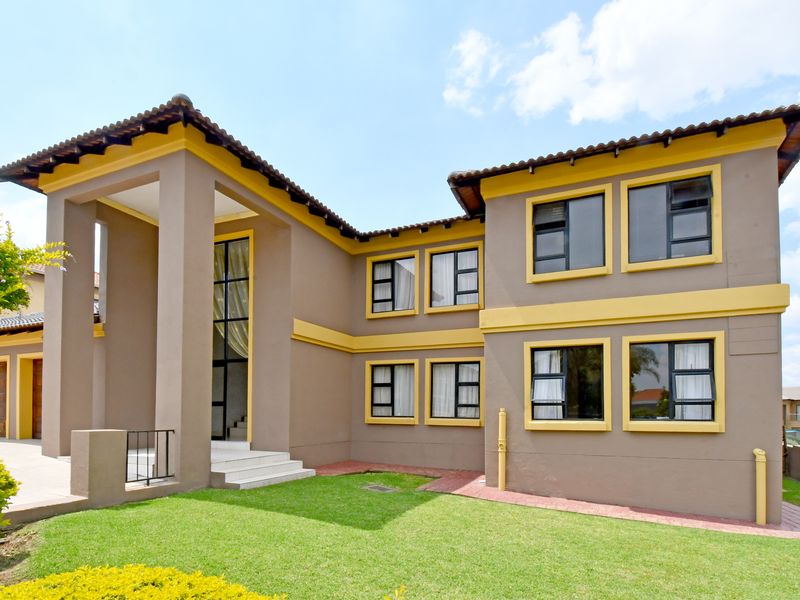 A well-maintained double-storey residential property featuring a prominent covered entrance, tiled roof, and modern aluminium-framed windows set against a landscaped garden.