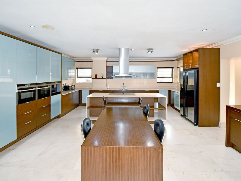 Spacious modern kitchen featuring extensive cabinetry, a central island with integrated cooktop, built-in appliances, and stone flooring.
