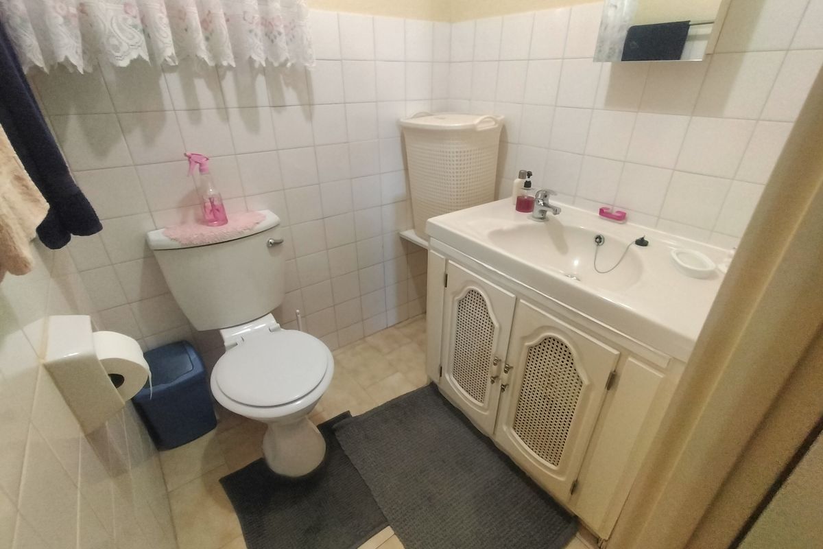 A functional bathroom featuring a vanity cabinet with integrated basin, toilet, and wall tiling. The space is dated and would benefit from modern updates.