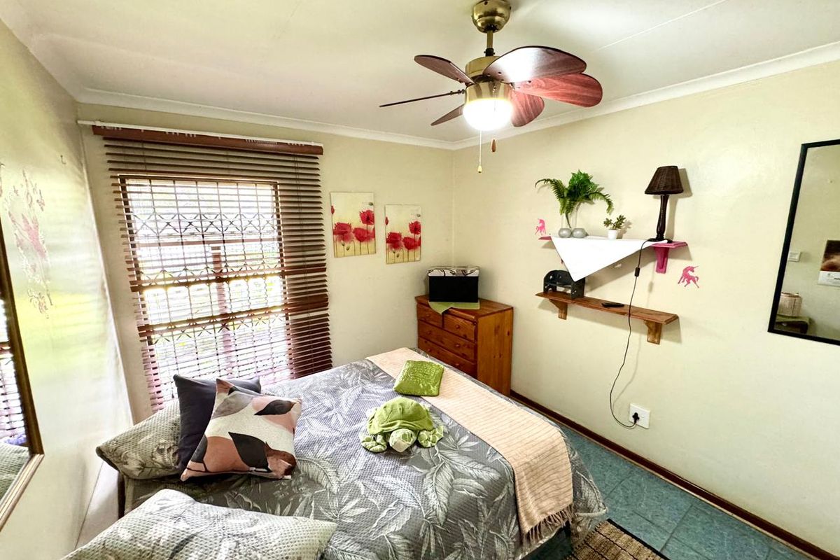 A cozy bedroom featuring a ceiling fan, wooden blinds, and tiled flooring, providing a functional and comfortable living space.