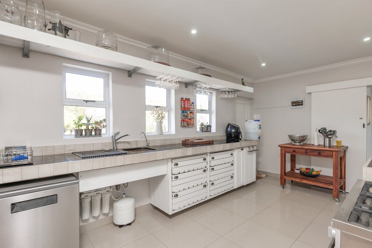 A functional kitchen featuring tiled countertops, an undermount sink with a water filtration system, floating shelving, and a gas hob.