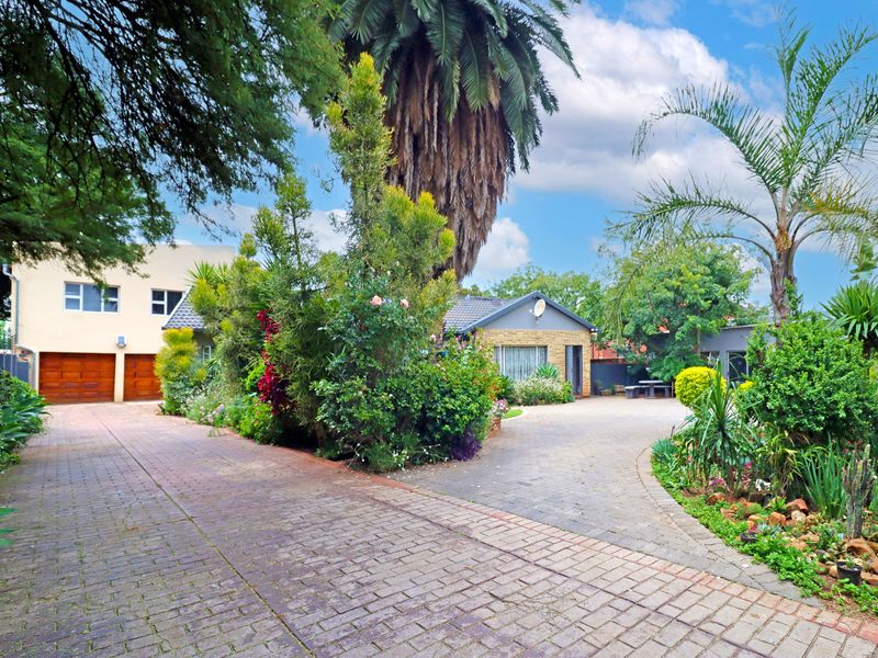 Front view of the property featuring a spacious paved driveway, established garden, and a double garage with wooden doors.