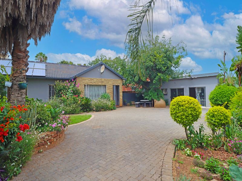 Front view of the property featuring a paved driveway, established garden, brick facade detailing, and roof-mounted solar panels.