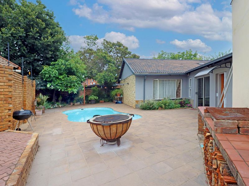 Rear garden area featuring a swimming pool, paved patio, and a built-in brick braai, ideal for outdoor entertaining.