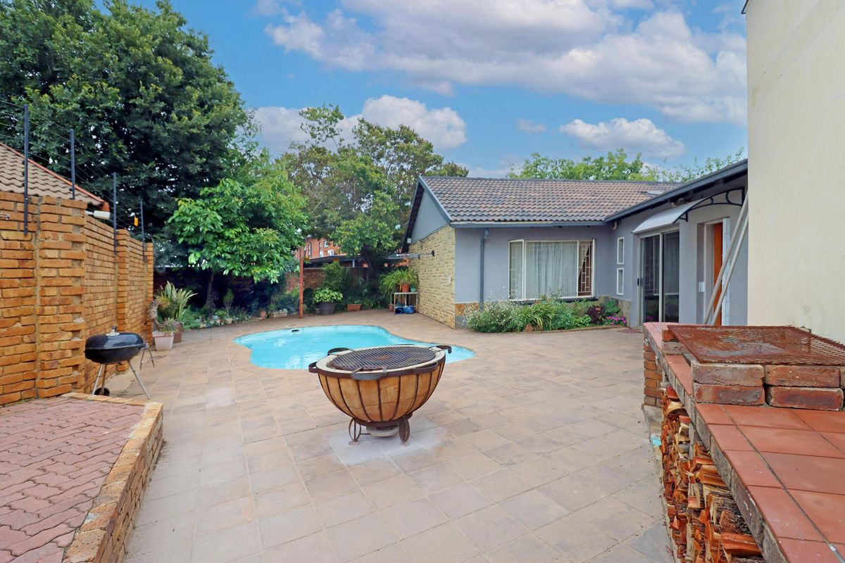 Rear garden area featuring a swimming pool, paved patio, and a built-in brick braai, ideal for outdoor entertaining.