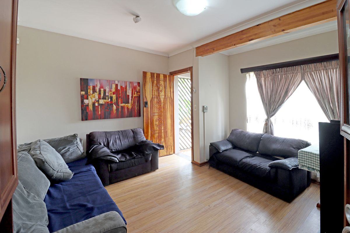 A living room featuring laminate flooring, an exposed timber ceiling beam, and a solid timber door leading to an exterior security gate.