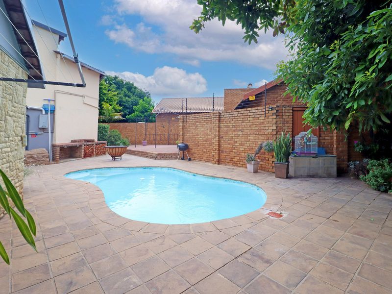 Outdoor pool area featuring a paved patio, built-in braai, and brick boundary walls with electric fencing.