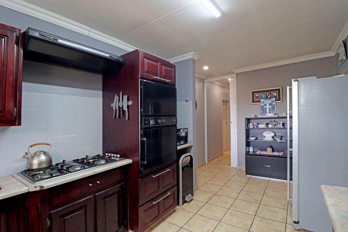 A functional kitchen featuring dark wood cabinetry, a gas hob with extractor fan, built-in oven, and tiled flooring with a neutral wall finish.